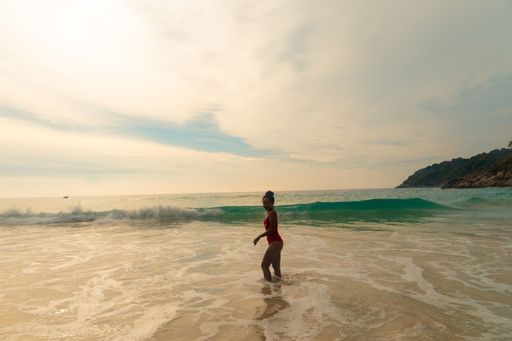 A beautiful shot of a female wearing a red swimsuit standing at the ocean shore during sunset