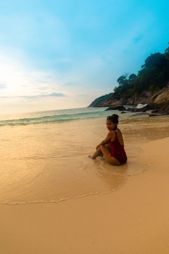 A vertical shot of a female wearing a red swimsuit sitting and relaxing at the sandy beach