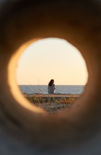 A vertical shot of a woman standing on the beach seen through a pipe