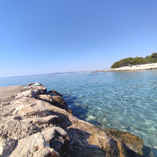 A rocky beach by tranquil water and a green hill on the other side under blue sky