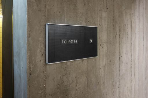 A closeup shot of a small informative board and an arrow pointing to the toilettes