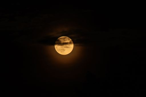 The glowing yellow full moon covered by dark clouds in a night sky