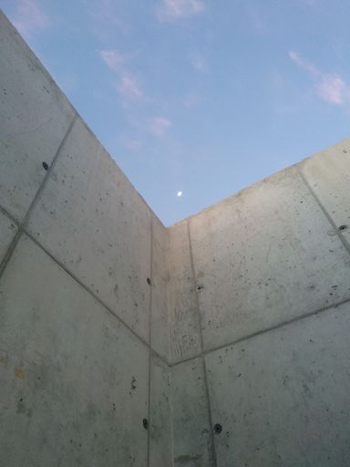 A vertical shot of a wall with the moon visible in the sky during the afternoon