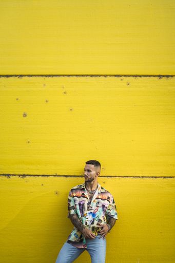 A vertical shot of a European male with tattoos leaning against a yellow building