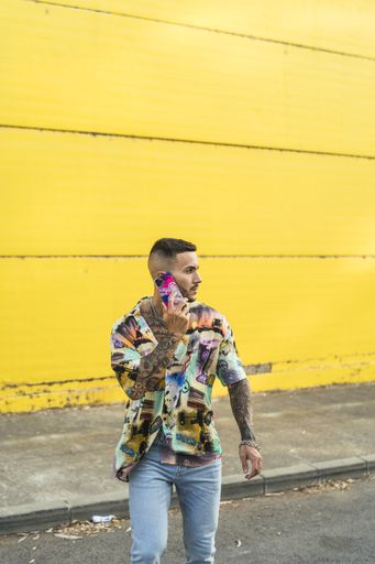 A vertical shot of a young Caucasian man with tattoos on a yellow background