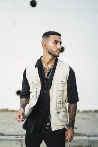 A shallow focus of a young male with tattoos wearing a black shirt with a white jacket