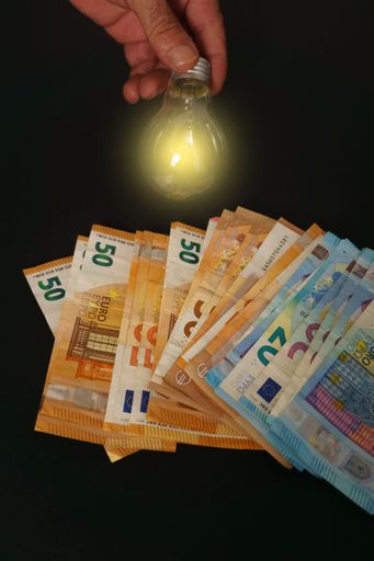 lighted light bulb with euro banknotes in the background on a black background, concept of rising electricity prices