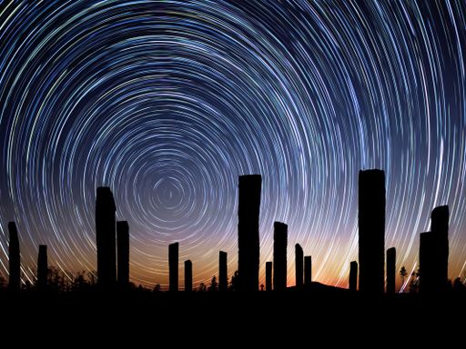 The silhouettes of wooden pillars with circle star trail in blue and orange sky, long exposure