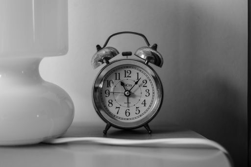 A grayscale shot of a tabletop featuring a decorative vintage alarm clock