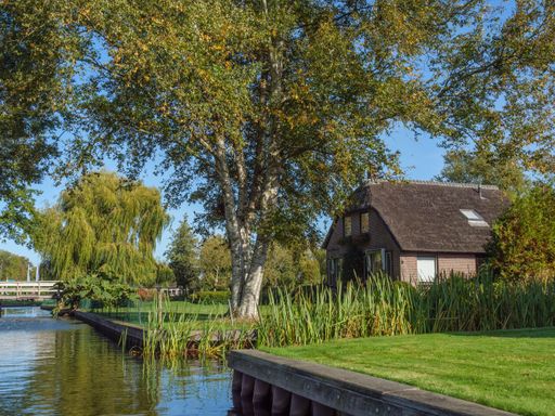 An image of the water surface of the gracht located in Giethoorn, Netherlands and surrounded with grass and a house