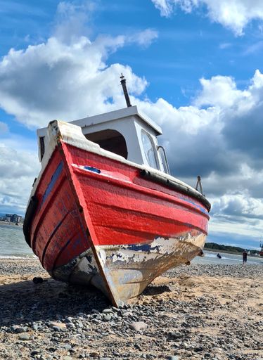 A vertical shot of an old, damaged boat at the beach under the clouds