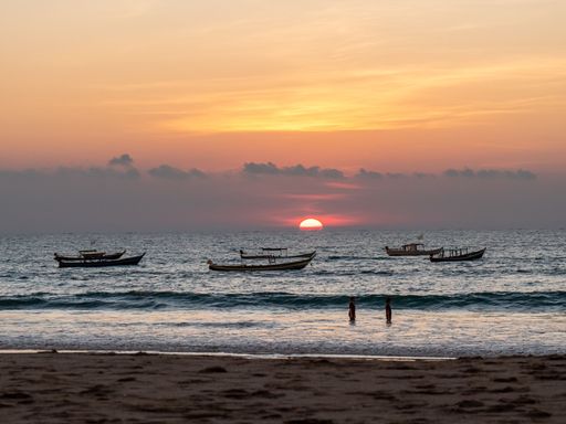 A beautiful red sunset over the Bay of Bengal and people and boats in the water in Ngwesaung, Myanmar