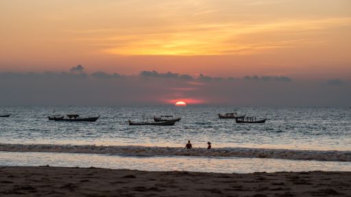 A beautiful red sunset over the Bay of Bengal and people and boats in the water in Ngwesaung, Myanmar
