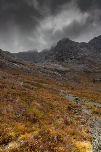 A vertical shot of a person climbing a mountain with a stormy sky in the background