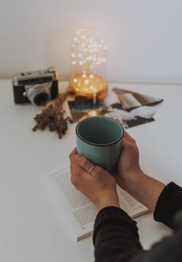 A vertical shot of a person holding a mug with a book, camera, lantern and photos on a table