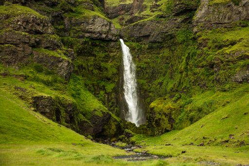 A waterfall dropping from rocky mountain covered by nature in Iceland