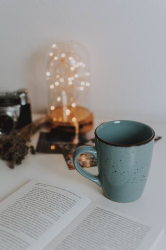 A vertical shot of a book, a mug, lantern, a camera on a white table
