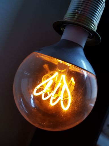 A vertical shot of a lit light bulb hanging from the ceiling