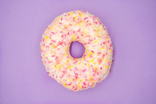 A top view of a delicious glazed donut with sprinkles isolated on a purple background
