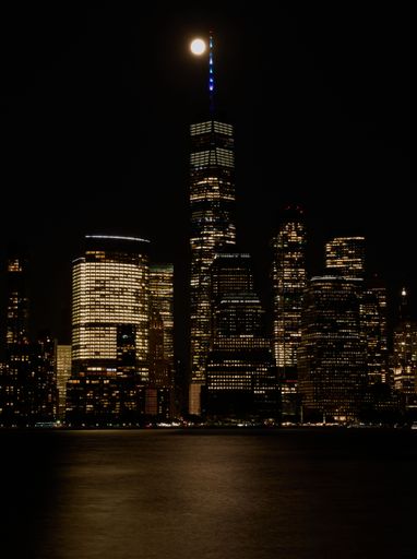 A vertical shot of a full moon over One World Trade Center at night