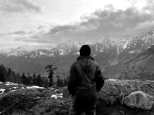 A grayscale shot of a hiker enjoying the view from a mountain summit in Manali, India