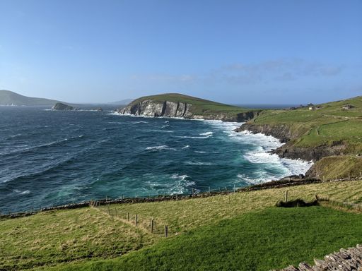 A scenic shot of foamy waves crashing the green shore under the blue sky in Ireland