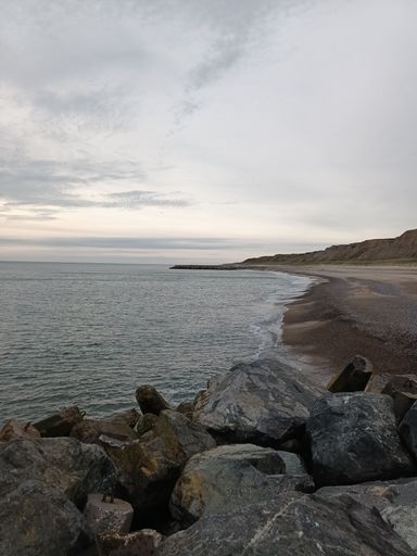 A vertical shot of the sea with huge rocks on the shore on a cloudy day