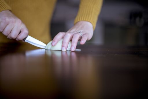 A closeup shot of a female slicing up onion on a wooden surface with a blurred background