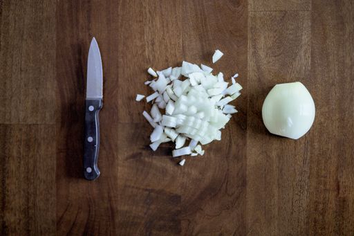An overhead shot of a knife near chopped and sliced onion on a wooden surface