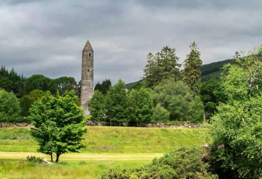 The Round Tower surrounded by green trees against the background of the cloudy sky. Glendalough.