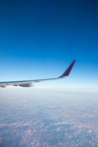 A vertical closeup shot of a wings of an airplane in white and red colors above the clouds