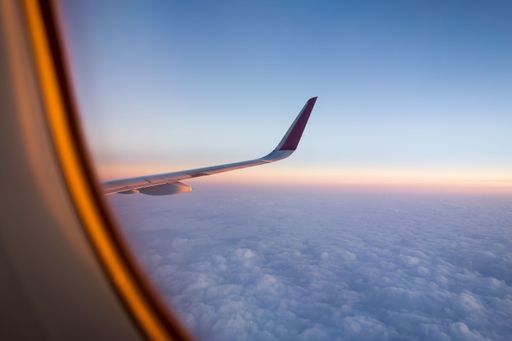 A closeup shot of the wing of an airplane from an aisle seat and the sky at sunset