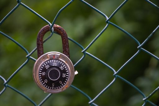 A closeup shot of a rusty lock hanging from a wired fence