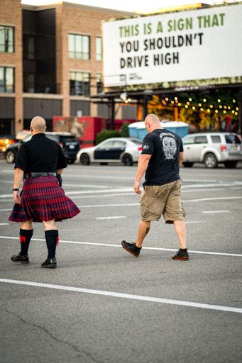 A vertical shot of two men on a street and one of them is wearing a kilt