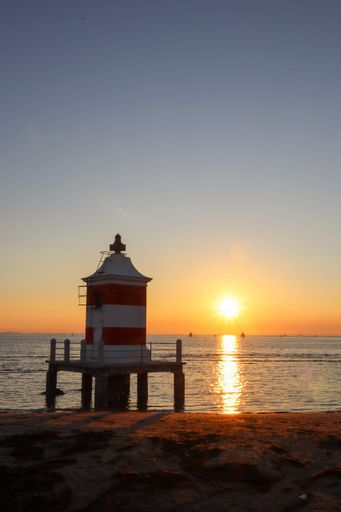 A vertical shot of the shiny sea with a lighthouse at scenic sunrise, Italy