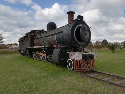 An old locomotive monument located at the edge of town in a green field under the cloudy sky