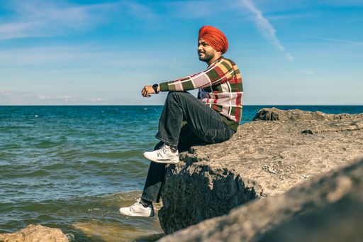 A South Asian male with red turban cap sitting on rock formation overlooking the sea