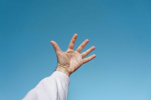 A closeup of a hand with a white sleeve reaching the blue sky