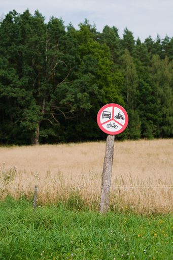 A vertical shot of a round three-part road sign banning cars, bikes and motorcycles in the countryside