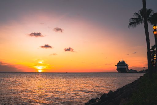 A gorgeous sunrise at sea with an orange sky in a pink sky over a huge boat surrounded by palm trees
