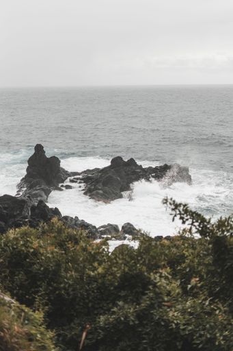 A beautiful vertical shot of vicious tides crashing against huge rocks in the ocean on a gloomy day