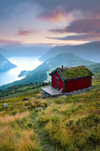 A vertical shot of a mountain cabin overlooking a fjord at sunset, Norway