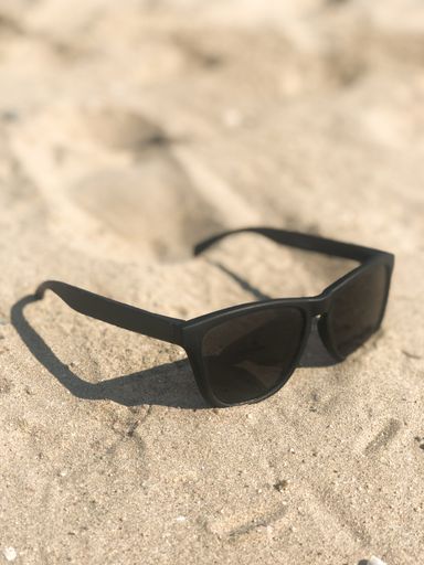 A vertical shot of a pair of sunglasses on the sand