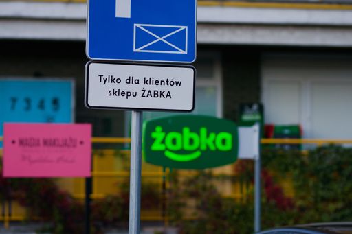 a parking sign "only for clients of Zabka shop" in polish with Zabka logo in the background, a selective focus shot