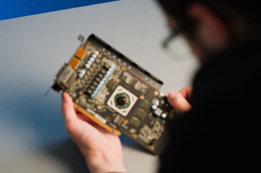 A man in glasses holding a graphics card GPU AMD with his eye reflected in the core, selective focus
