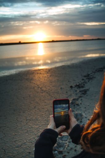 A young woman taking sunset photos with her phone at the lakeside