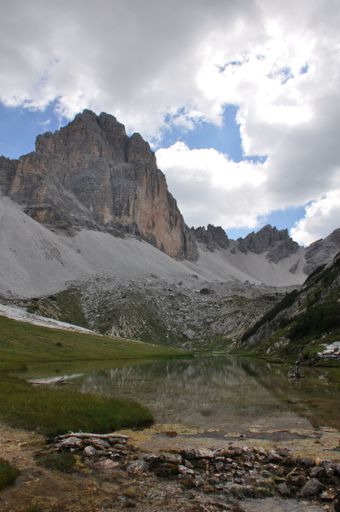 A vertical shot of a lake in a valley among rugged and rocky mountains, dense white clouds in the sky