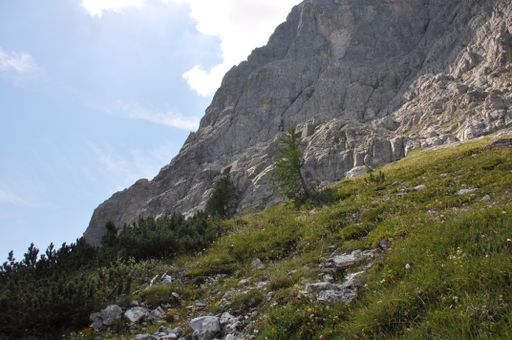 The rugged rocky mountain and a gentle slope covered with stones and green plants on a sunny day