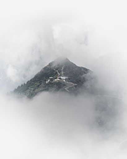 A vertical shot of a misty mountain with buildings surrounded with thick fog