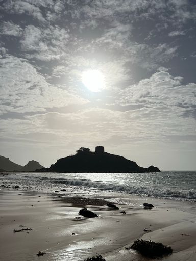 A vertical shot of a sandy beach against sea waves and an island on a sunny day